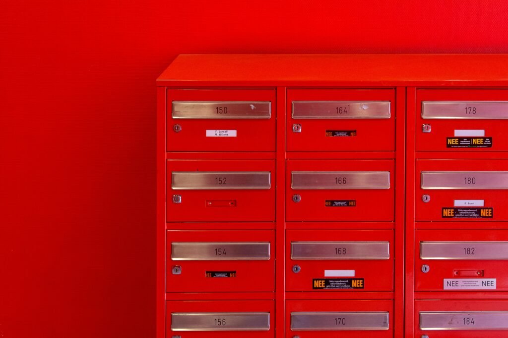 A row of sleek red mailboxes with metallic number panels and keyholes against a red background.