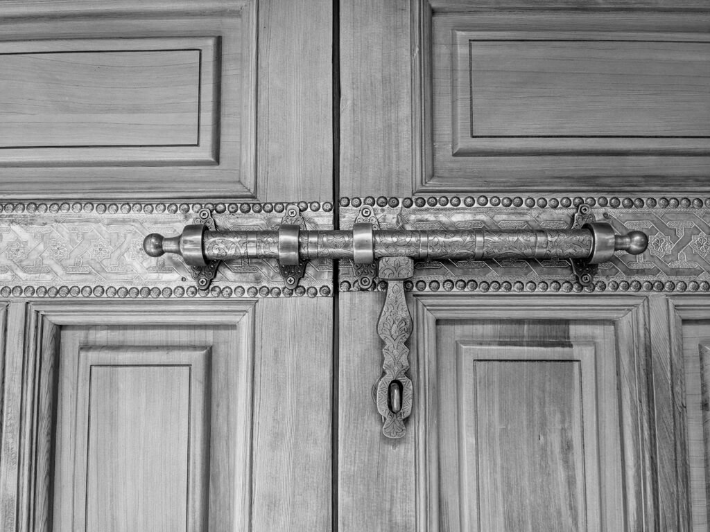 Quincaillerie de porte : Le guide complet pour allier esthétique premium et haute sécurité Close-up of an intricately carved wooden door with an ornate metal bolt in Morocco.