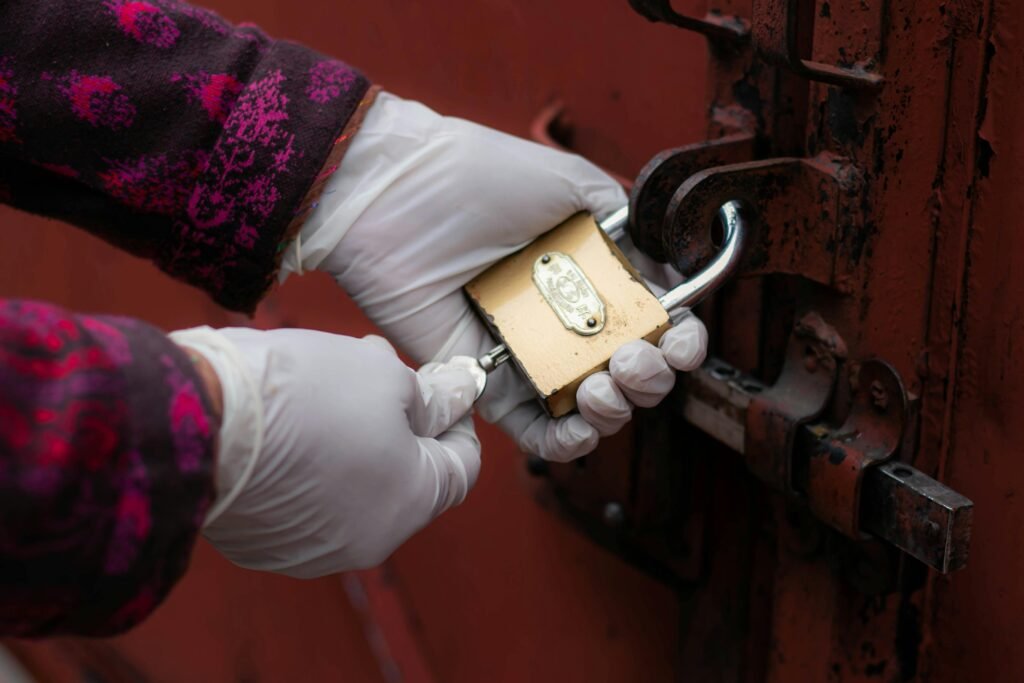 A close-up of gloved hands unlocking a rusty door padlock.