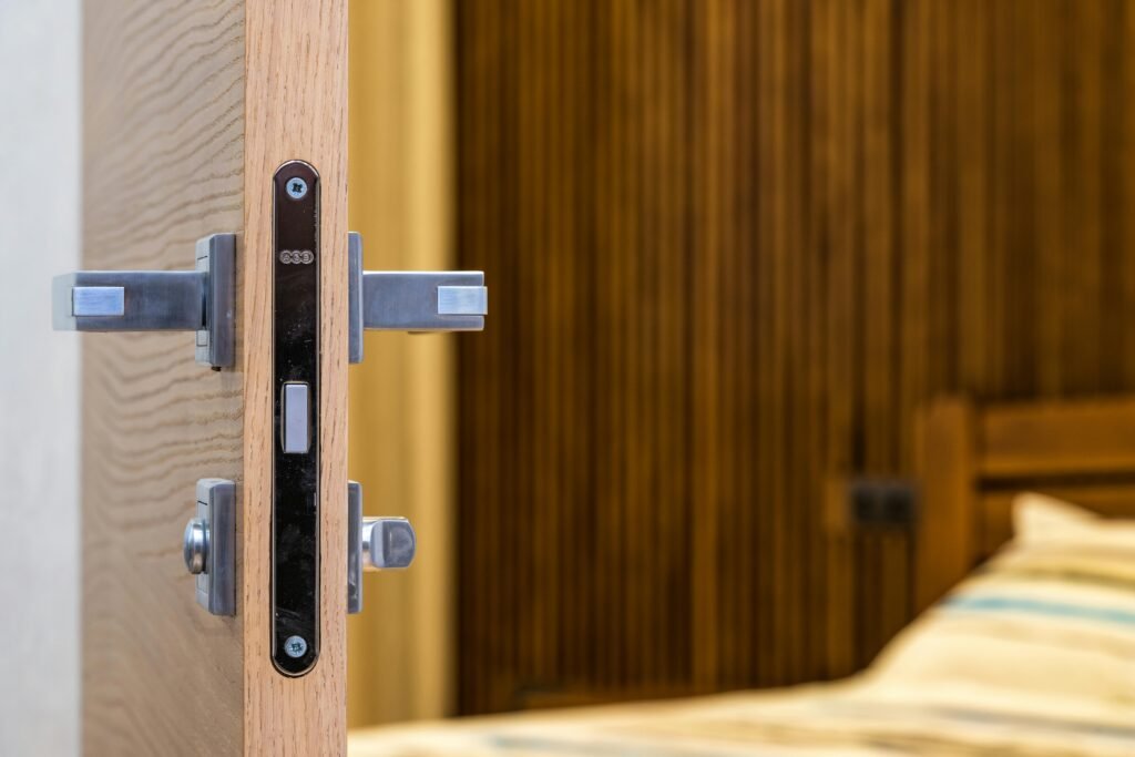 Opened doorway with lock and simple metal handle in light room with wooden bed