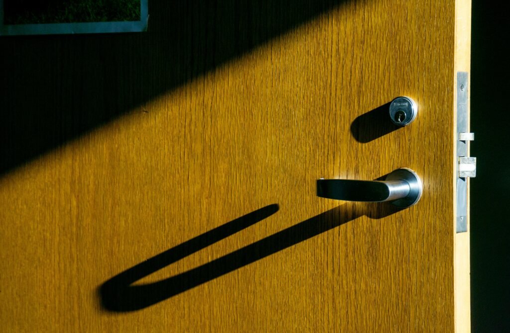 Close-up of a wooden door with a metal handle casting a shadow in the sunlight.