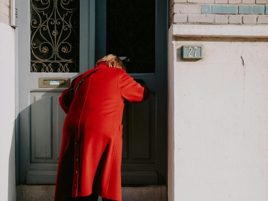 A person in a red coat enters a distinctive blue door with ornate decoration.