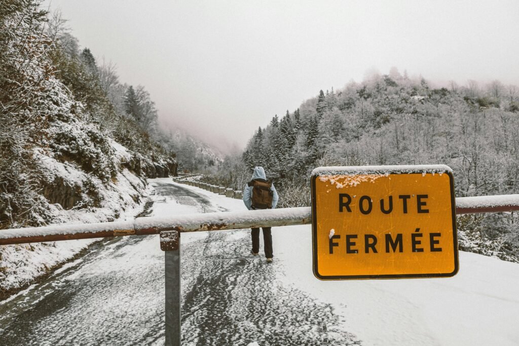 A lone backpacker on a snowy mountain road with a 'Route Fermée' sign.