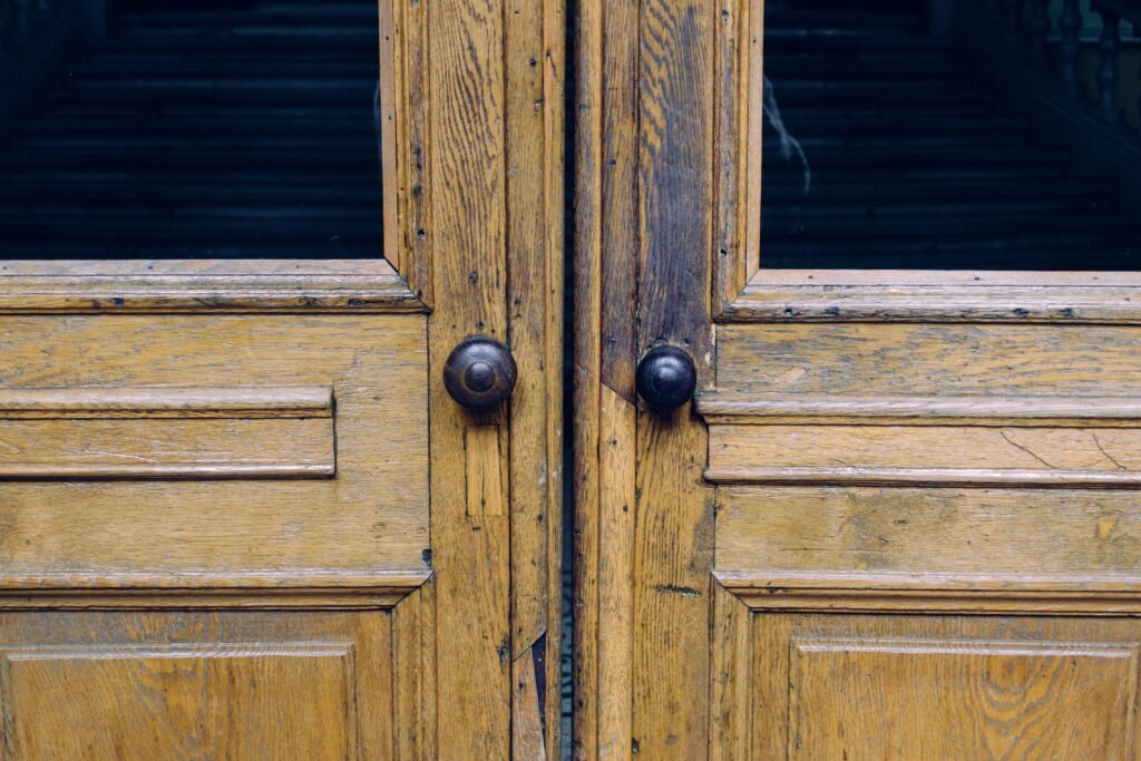 Close-up of rustic wooden double doors featuring antique metal knobs and natural weathered textures.