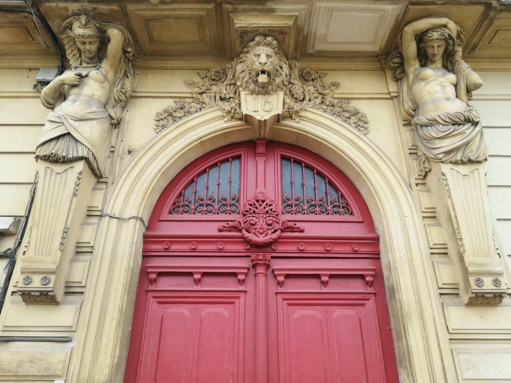 Stunning red door with intricate sculptures and a lion motif on a classic facade.