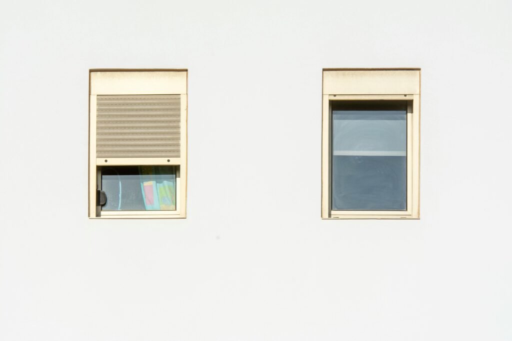 Protéger ses fenêtres : Les solutions de serrurerie complémentaires A minimalistic facade featuring two modern windows with shutters in a bright, contemporary style.